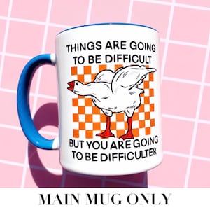 May include: White ceramic mug with a blue handle and rim. The mug features a cartoon goose illustration on an orange and white checkered background. Text on the mug reads "THINGS ARE GOING TO BE DIFFICULT BUT YOU ARE GOING TO BE DIFFICULTER."