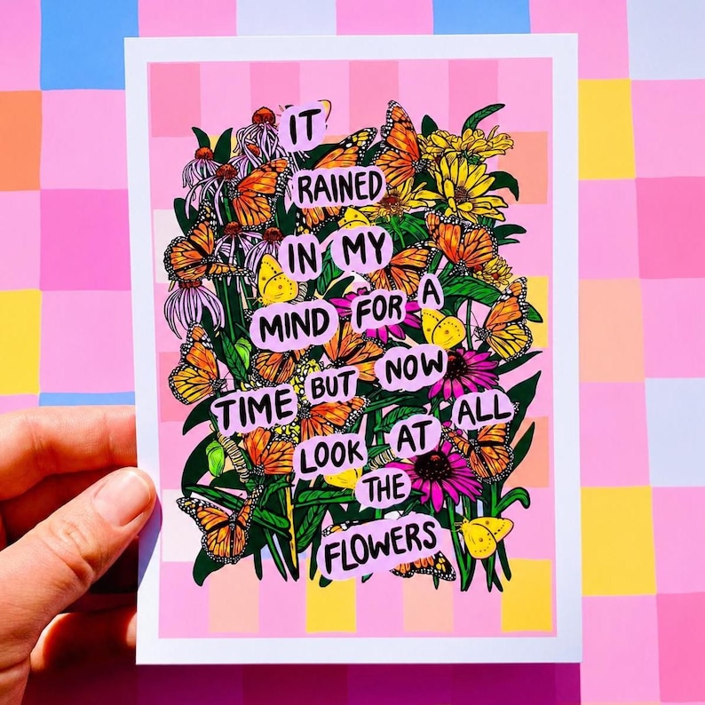 May include: A pink and white art print featuring a floral and butterfly design. The print includes the text "It rained in my mind for a time but now look at the flowers". The artwork has a pink and yellow checkered background.