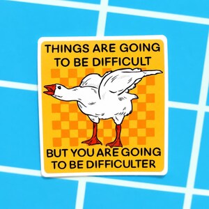 May include: A sticker with a white goose illustration on a yellow background with orange squares. The sticker reads "THINGS ARE GOING TO BE DIFFICULT" and "BUT YOU ARE GOING TO BE DIFFICULTER" in black text. The sticker is on a blue background.