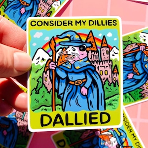 Puede incluir: Una pegatina con una ilustración de un hámster vestido de mago, con una túnica y sombrero azules, sosteniendo un bastón. El texto "CONSIDER MY DILLIES" y "DALLIED" está en amarillo y blanco.