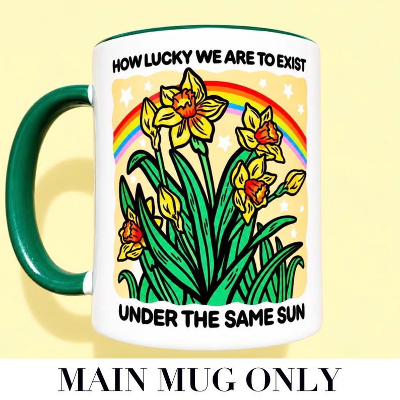 May include: A white ceramic mug with a dark green handle and rim, featuring a colorful illustration of yellow daffodils, green leaves, and a rainbow against a pale yellow background, with the text "HOW LUCKY WE ARE TO EXIST UNDER THE SAME SUN".
