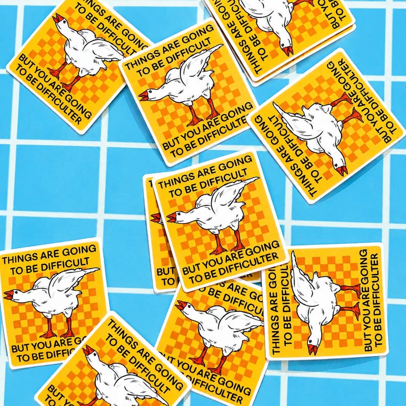 May include: A collection of yellow stickers with a white goose illustration and the text "THINGS ARE GOING TO BE DIFFICULT" and "BUT YOU ARE GOING TO BE DIFFICULTER" in black. The stickers are scattered on a blue tiled surface.