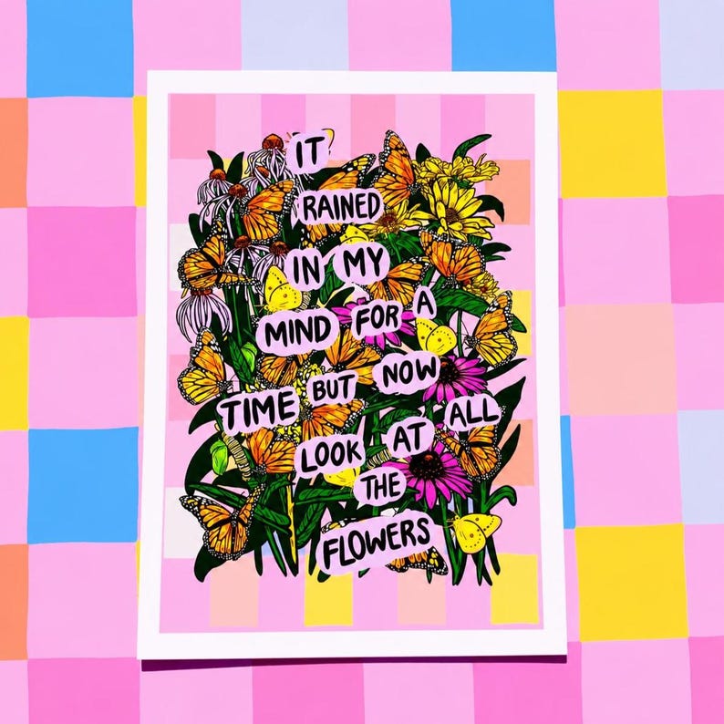 May include: A framed art print with a pink and white striped background. The artwork features a vibrant arrangement of butterflies and flowers, with the text "IT RAINED IN MY MIND FOR A TIME BUT NOW LOOK AT THE FLOWERS."