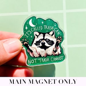 May include: A clear acrylic magnet featuring a raccoon illustration with the text "IT'S CALLED TRASH CAN NOT TRASH CANNOT" in white. The raccoon is black and white with a green background.