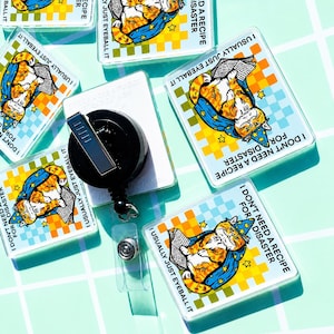 May include: Square badge reels featuring a cartoon orange cat wearing a blue wizard hat and cape, reading a book. The design includes a yellow and light blue checkered background with the text I DON'T NEED A RECIPE FOR DISASTER and I USUALLY JUST EYEBALL IT.