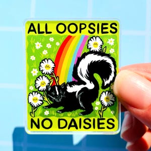 May include: A square sticker with a cartoon skunk illustration. The skunk is black and white, with a rainbow and daisies in the background. The text reads "ALL OOPSIES NO DAISIES" in a green border.