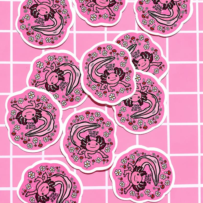 May include: A collection of pink axolotl stickers. Each sticker features a pink axolotl with a long, curved tail, surrounded by flowers and mushrooms. The text "LET ME BE WEIRD IN PEACE" is included on each sticker.