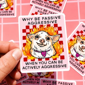 May include: A pink sticker with the text "WHY BE PASSIVE AGGRESSIVE WHEN YOU CAN BE ACTIVELY AGGRESSIVE." The sticker features a cartoon chihuahua with flames around its head and a heart-shaped collar.