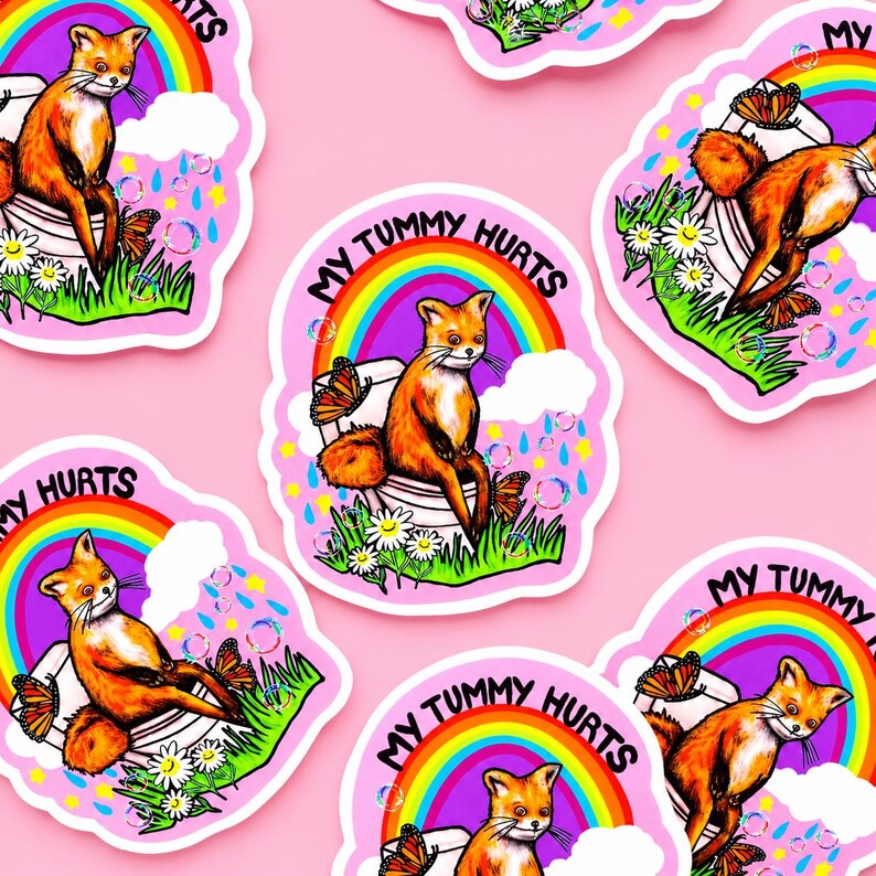 May include: A die-cut sticker featuring an orange fox sitting on a white toilet, surrounded by a vibrant rainbow, green grass, white daisies, butterflies, and bubbles. The text MY TUMMY HURTS is printed in black letters above the rainbow arch.