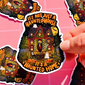 May include: A sticker with a spooky haunted house illustration. The house is decorated with lights, pumpkins, and ghosts. The text on the sticker reads "It's Not Just a Haunted House, It's a Haunted Home."
