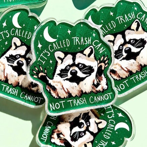 May include: A collection of green, raccoon-shaped stickers. Each sticker features a raccoon illustration with the text "IT'S CALLED TRASH CAN NOT TRASH CANNOT" in white. The background is a dark green with a crescent moon and stars.