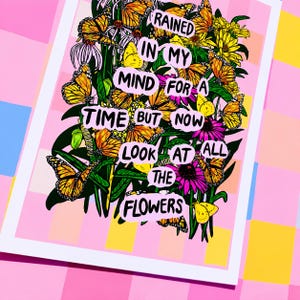 May include: A framed art print featuring a vibrant floral arrangement with monarch butterflies. The artwork includes text that reads "Rained in my mind for a time but now look at all the flowers." The print has a pink and white border.