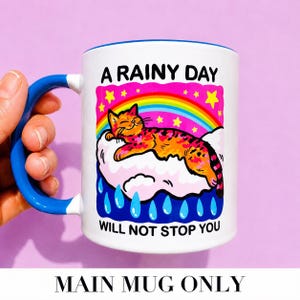 May include: A white ceramic mug with a blue handle and interior. The graphic features an orange tabby cat sleeping on a pink cloud under a rainbow and yellow stars, with blue raindrops below. The text reads A RAINY DAY WILL NOT STOP YOU.