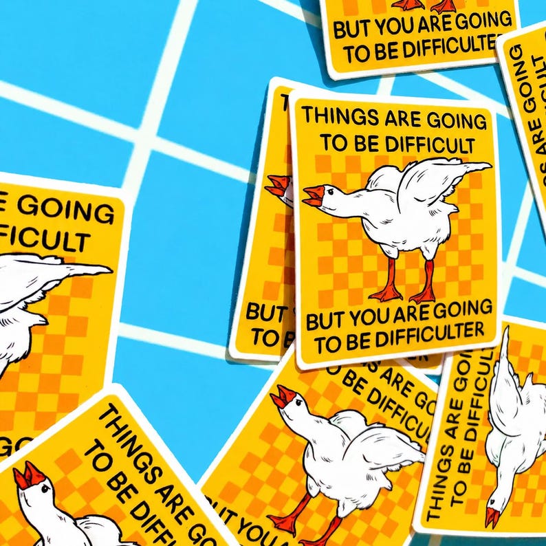 May include: A collection of yellow stickers with a white goose illustration and the text "THINGS ARE GOING TO BE DIFFICULT" and "BUT YOU ARE GOING TO BE DIFFICULTER". The stickers have a checkered background and are scattered on a blue surface.