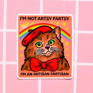 Pu&ograve; includere: Un adesivo quadrato raffigurante un gatto marrone che indossa un basco rosso e un papillon rosso. Sopra il gatto ci sono un arcobaleno e stelle gialle su sfondo color pesca. Il testo recita I'M NOT ARTSY FARTSY e I'M AN ARTISAN FARTISAN.