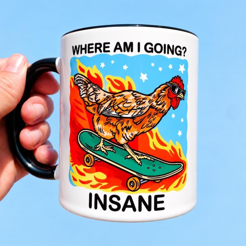 May include: A white ceramic mug with a black handle and rim featuring a graphic of a brown chicken wearing sunglasses on a green skateboard. The background shows orange flames and white stars against a blue sky. Text reads WHERE AM I GOING? and INSANE.
