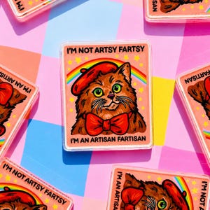 May include: Rectangular sticker with a cartoon cat wearing a red beret and bow tie, set against a rainbow and stars. The text reads "I'M NOT ARTSY FARTSY, I'M AN ARTISAN FARTISAN". The sticker is surrounded by similar stickers.