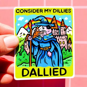 Könnte beinhalten: Ein farbenfroher Aufkleber mit den Texten "CONSIDER MY DILLIES" und "DALLIED". Er zeigt ein Cartoon-Opossum als Zauberer mit Stab, vor einem Hintergrund aus Regenbogen und Burg. Das Design ist auffällig und bunt.