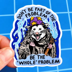 May include: A sticker depicting an opossum in a wizard's hat and holding a staff. The text on the sticker reads "DON'T BE PART OF THE PROBLEM BE THE *WHOLE* PROBLEM" in a blue and white design with lightning bolts and stars.