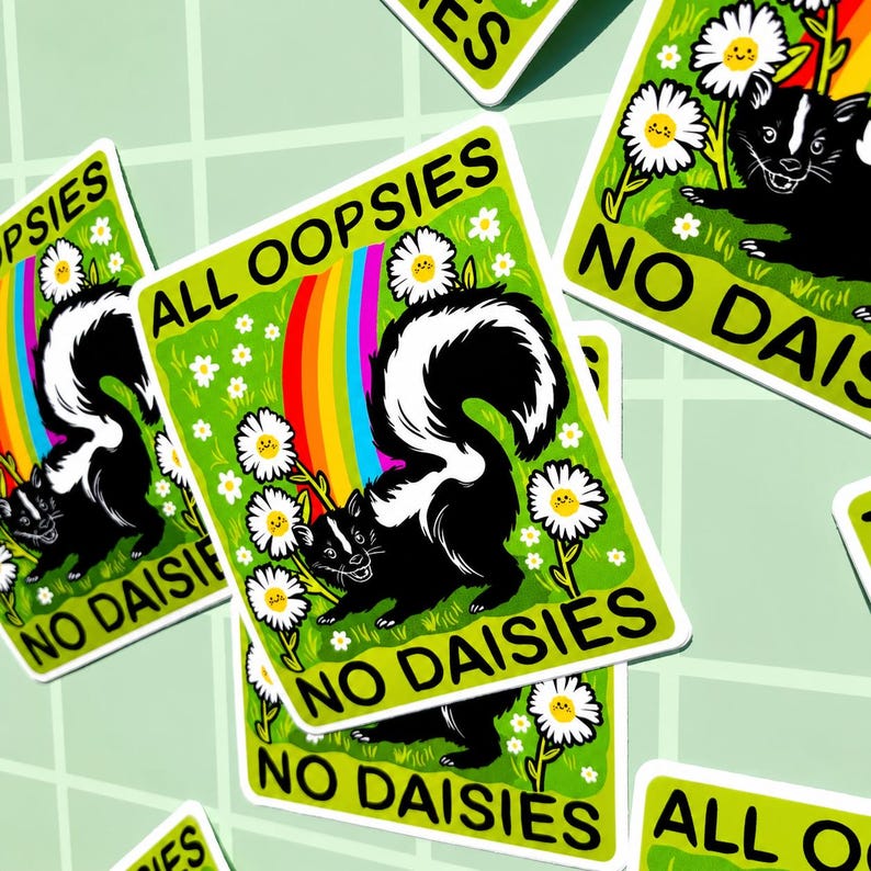 May include: A rectangular sticker featuring a black and white skunk standing in a green field with white daisies and a colourful rainbow. The text ALL OOPSIES is printed at the top and NO DAISIES is printed at the bottom in bold black letters.
