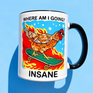 Puede incluir: Una taza de cer&aacute;mica blanca con asa y borde negros que presenta un gr&aacute;fico de un pollo naranja con gafas de sol sobre un monopat&iacute;n verde entre llamas naranjas y estrellas blancas. El texto dice WHERE AM I GOING? y INSANE.
