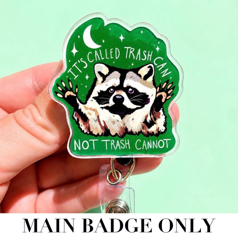 May include: A clear acrylic badge reel featuring a green background with a raccoon illustration. The text reads IT'S CALLED TRASH CAN NOT TRASH CANNOT. The design includes a white crescent moon and small stars, with a metal clip and clear plastic strap.