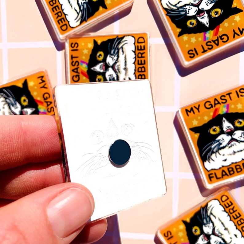 Puede incluir: Imanes cuadrados con un dise&ntilde;o de gato en blanco y negro. Los imanes tienen texto que dice "MY GAST IS FLABBERED" y "BERED" sobre un fondo naranja con estrellas. Un im&aacute;n se sostiene en una mano.