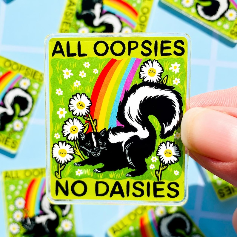 May include: A rectangular acrylic sticker featuring a black and white skunk standing in a green field with white daisies and a rainbow. The text ALL OOPSIES is printed in black at the top, and NO DAISIES is printed in black at the bottom.