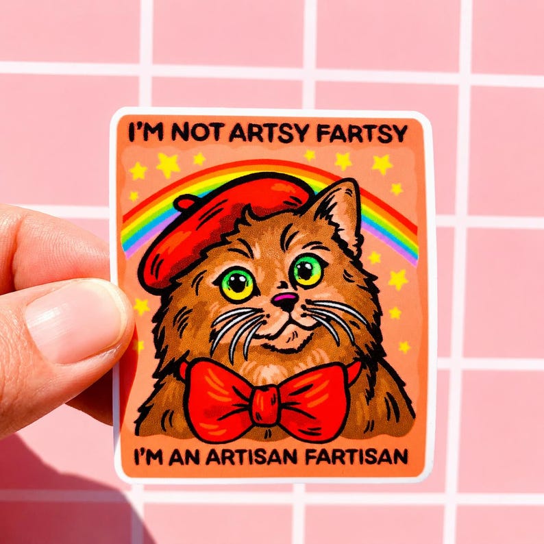 Pu&ograve; includere: Un adesivo rettangolare con un gatto marrone che indossa un basco rosso e un papillon rosso. Sopra il gatto ci sono un arcobaleno e stelle gialle su sfondo arancione. Il testo recita I'M NOT ARTSY FARTSY in alto e I'M AN ARTISAN FARTISAN in basso.