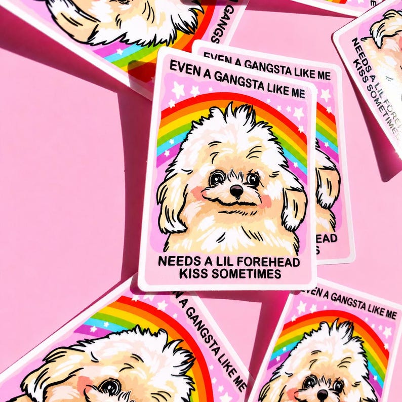May include: A rectangular sticker featuring a cartoon illustration of a fluffy white dog against a rainbow background. The text reads EVEN A GANGSTA LIKE ME NEEDS A LIL FOREHEAD KISS SOMETIMES. The sticker has a pink border and white stars.