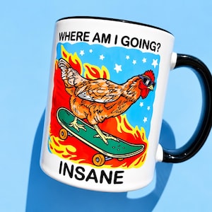 Puede incluir: Una taza de cer&aacute;mica blanca con asa y borde negros que presenta un gr&aacute;fico de un pollo marr&oacute;n con gafas de sol sobre un monopat&iacute;n verde. El fondo muestra llamas naranjas y estrellas blancas sobre un cielo azul. Texto: WHERE AM I GOING? e INSANE.
