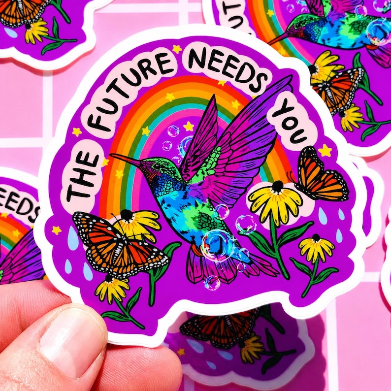 May include: A die-cut sticker featuring a vibrant, multi-colored hummingbird in flight, surrounded by yellow flowers, monarch butterflies, and a rainbow. The text THE FUTURE NEEDS YOU is printed in black, arched over the bird on a purple background.