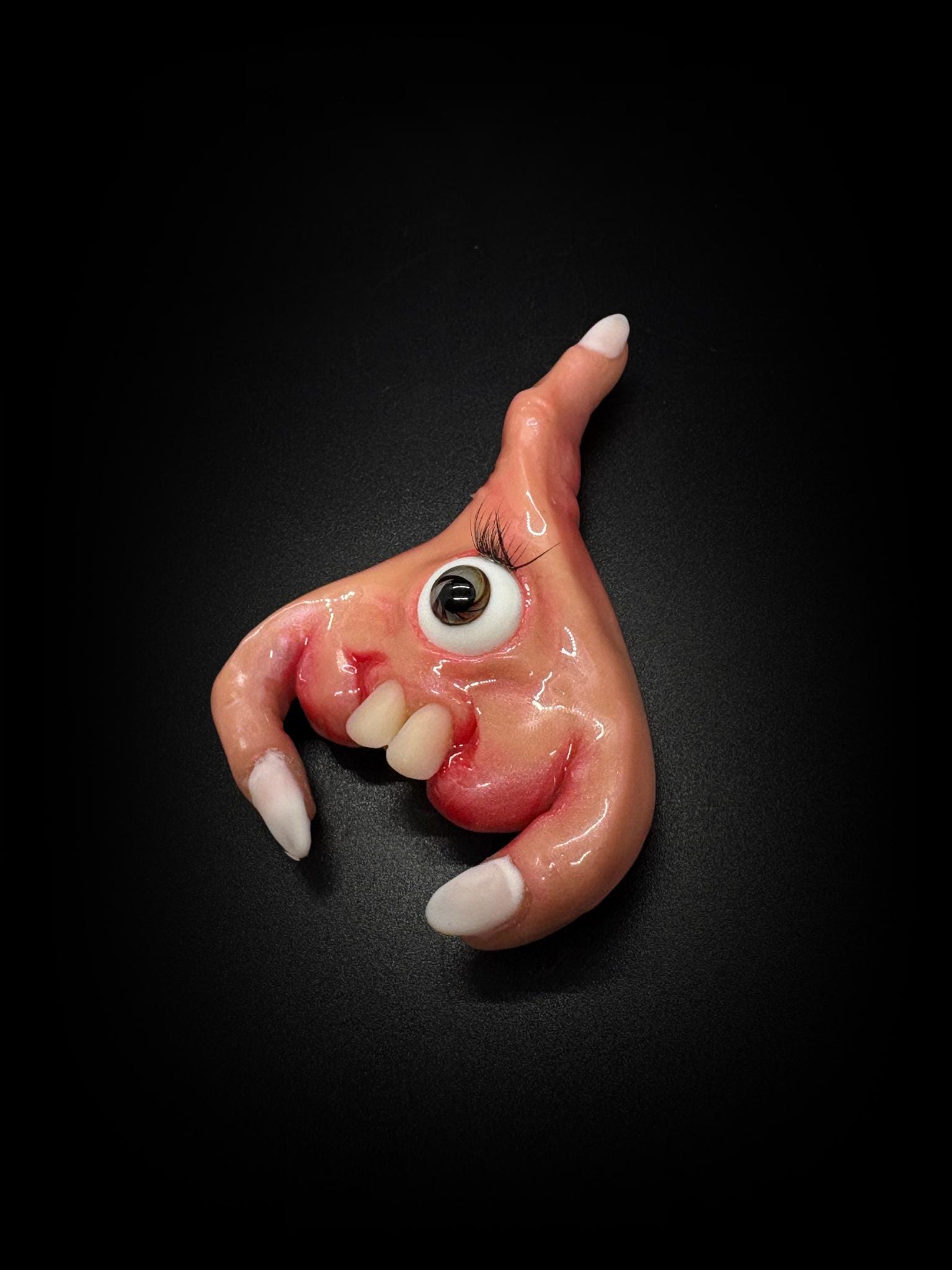 The Teratoma: a pink one-eyed fridge magnet with lashes, two teeth and three tiny fingers