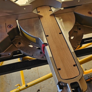 May include: A close-up of a miter saw with a wooden board in place. The saw is set at a 45-degree angle and the board is ready to be cut. The saw is silver and black with a yellow base.