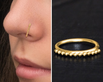 May include: Gold nose ring with a beaded design. The ring is made of a thin metal band with small, round beads evenly spaced along the band.