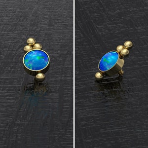 May include: Gold body jewelry with a blue opal gemstone and gold beads.