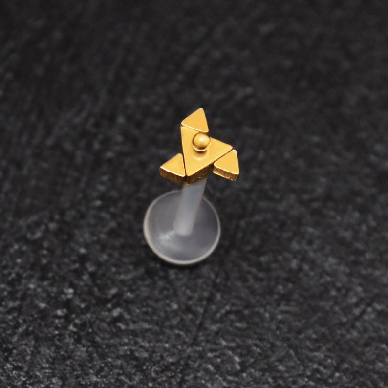 Puede incluir: Joyer&iacute;a corporal dorada con un dise&ntilde;o triangular. La joyer&iacute;a est&aacute; en un poste de pl&aacute;stico transparente.