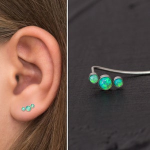 May include: A silver ear cuff with three green opal stones. The cuff is curved and has a delicate design.