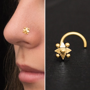 Puede incluir: Anillo de nariz de oro con un diseño en forma de estrella. La estrella está hecha de pequeñas cuentas redondas y tiene una forma triangular en el centro.
