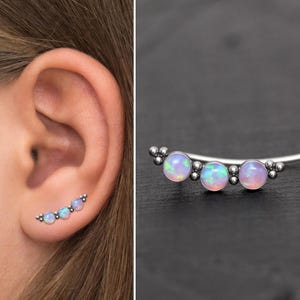 May include: A silver ear cuff with three iridescent opal stones. The cuff is curved and has a delicate design.