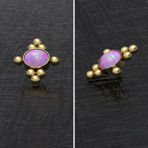 May include: A gold-colored body jewelry piece featuring a central oval-shaped, light purple opal stone. The opal is surrounded by a gold bezel and accented with small gold spheres. The piece is designed for body piercings.