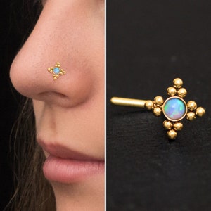 Puede incluir: Anillo de nariz de oro con una pequeña piedra de ópalo en el centro y un diseño geométrico de pequeñas cuentas doradas.