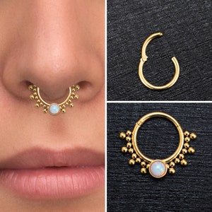 Könnte beinhalten: Goldener Septumring mit einem weißen Opal-Edelstein und einem Perlenmuster. Der Ring wird an der Nase eines Models gezeigt.