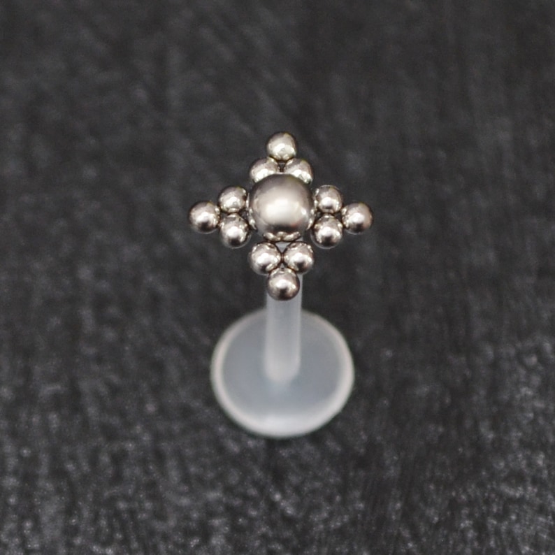 May include: A silver body piercing with a clear plastic post and a star-shaped top made of small silver balls.