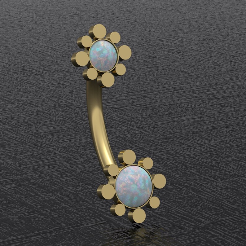 May include: Gold body jewelry with two opal gemstones set in a circular design with multiple smaller circles surrounding each stone.