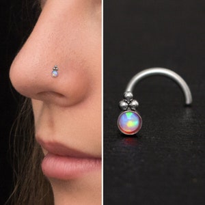 May include: A silver nose ring with a small opal gemstone and three silver beads. The ring is curved and has a small loop at the end.