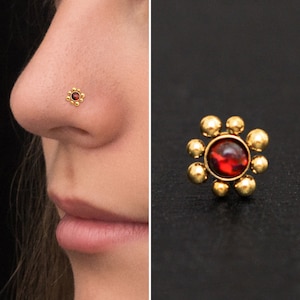 May include: Gold nose ring with a red gemstone in the center and a flower design around the stone.