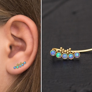 May include: A gold ear cuff with five iridescent opal stones. The cuff is curved and has a delicate design.