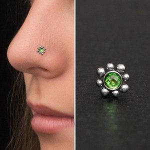 Könnte beinhalten: Ein silberner Nasenring mit einem grünen Edelstein in der Mitte, umgeben von kleinen silbernen Perlen. Der Ring hat die Form einer Blume.