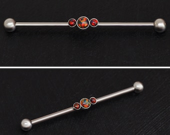 May include: A silver barbell with three red and orange opal-like gems. The barbell is 1.6 inches long.